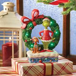 Visualiza al Grinch y su fiel perro Max junto a una gran corona navideña. En esta creación de Jim Shore, el Grinch, vestido como Santa Claus, sonríe sinceramente con un corazón más grande