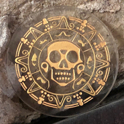Réplica de la moneda maldita del tesoro azteca basada en la saga de Piratas del Caribe. Esta moneda oficial está realizada en vidrio transparente con unas dimensiones aproximadas de 0.5 x 4 cm.
