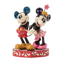 El encanto atemporal de Mickey y Minnie se materializa en esta pieza romántica de Jim Shore, donde cada trazo de rosemaling y los motivos patchwork realzan la complicidad de la pareja mientras posan sobre una base